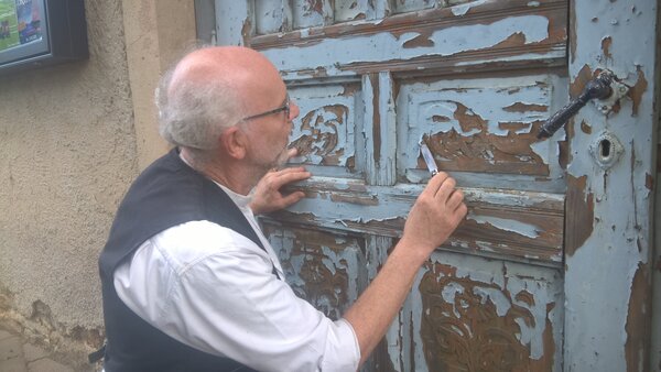 Ein Inspektor vor einer alten Holztür mit teilweise abbröckelnder Farbe