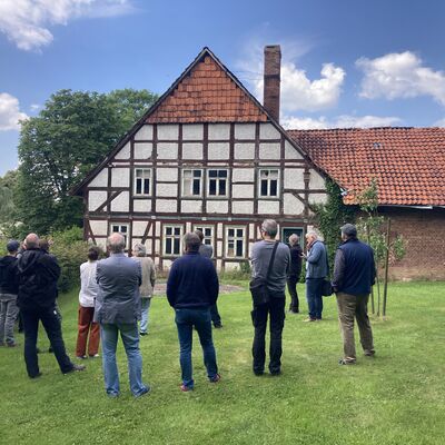 Bild vergr&ouml;&szlig;ern: Personen auf einer Wiese vor einem Fachwerkhaus mit angebautem Stall